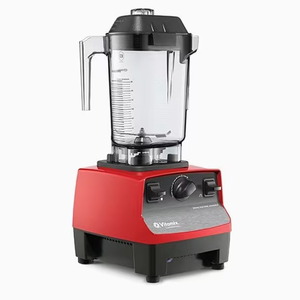 Un blender Vitamix roșu cu un borcan de plastic transparent, capac negru și butoane de control pe o bază argintie și neagră, prezentat pe un fundal alb.