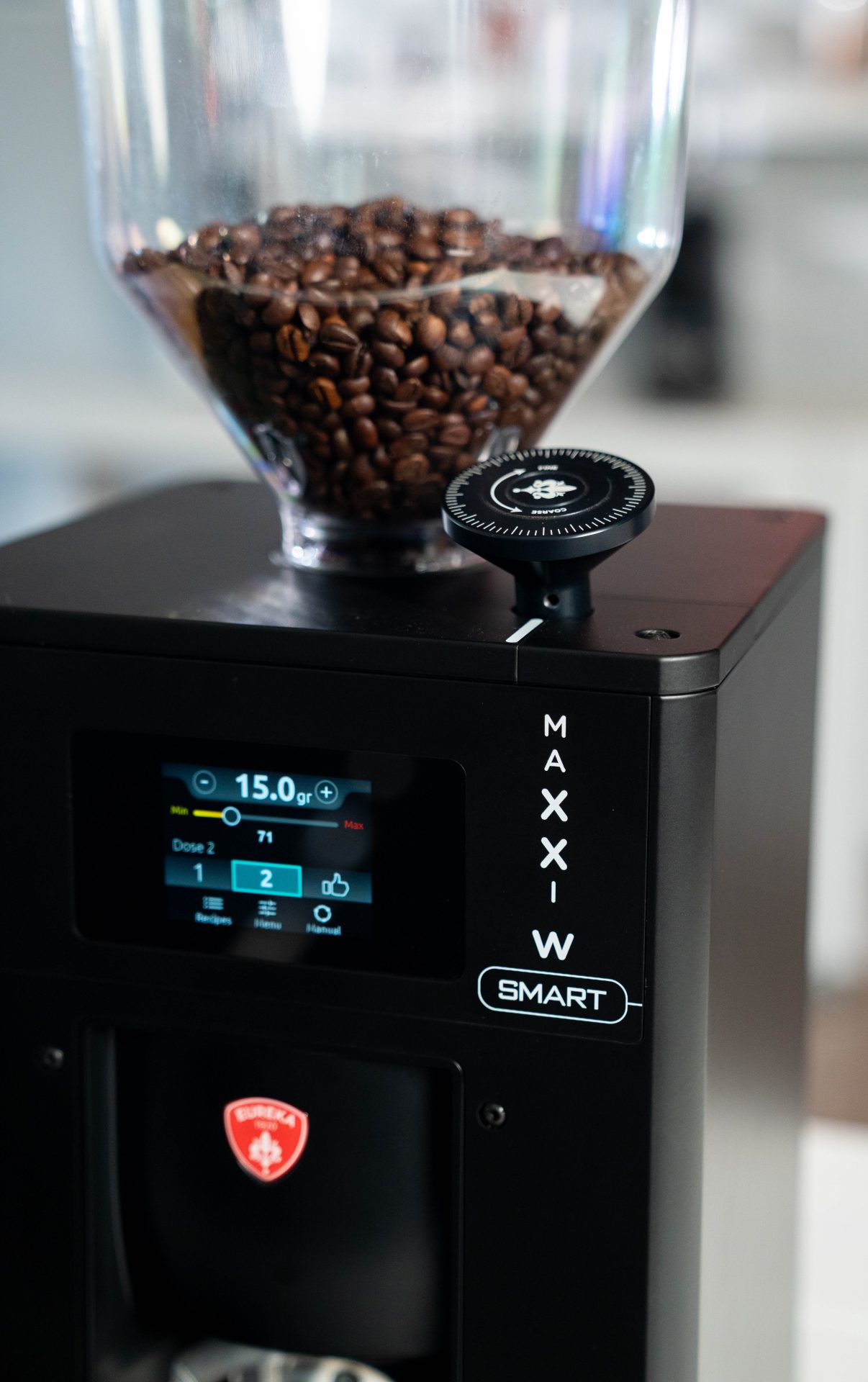 Un prim plan al unui măcinător de cafea plin cu boabe de cafea, care prezintă un afișaj digital cu setări și un cadran de reglare etichetat pe partea superioară a aparatului negru. Cuvântul SMART este vizibil pe panoul frontal al râșniței.