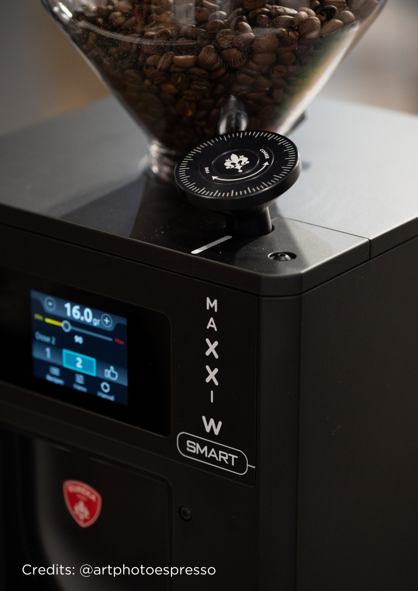 Un prim plan al unui râșniță de cafea modernă cu afișaj digital, un buncăr transparent plin cu boabe de cafea și un cadran de reglare a dimensiunii de măcinare. Cuvintele MAX, MIN și SMART sunt vizibile pe aparat. Credits: @artphotoespresso.